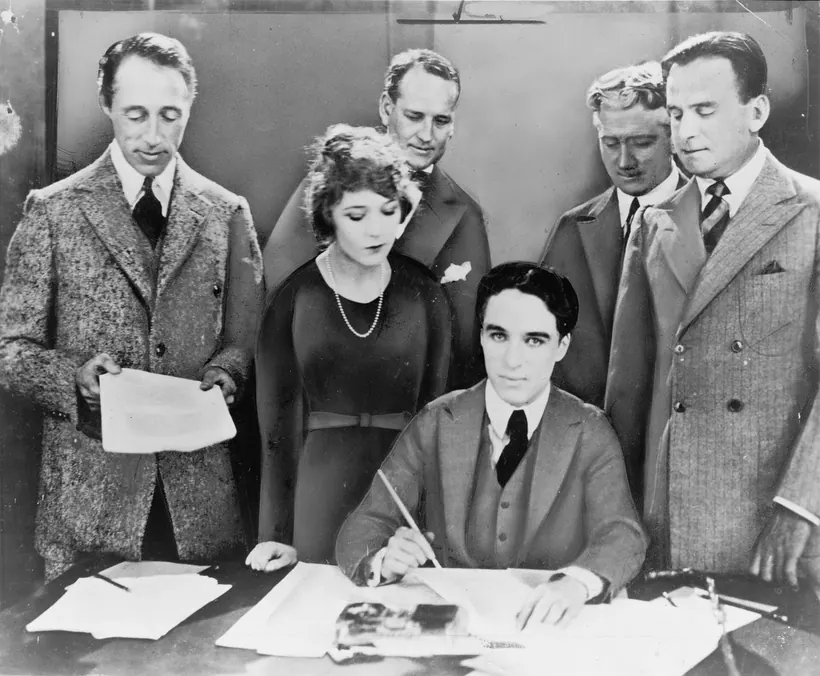 Four film artists seated at a table while two lawyers stand behind them at the 1919 signing of the contract that created United Artists